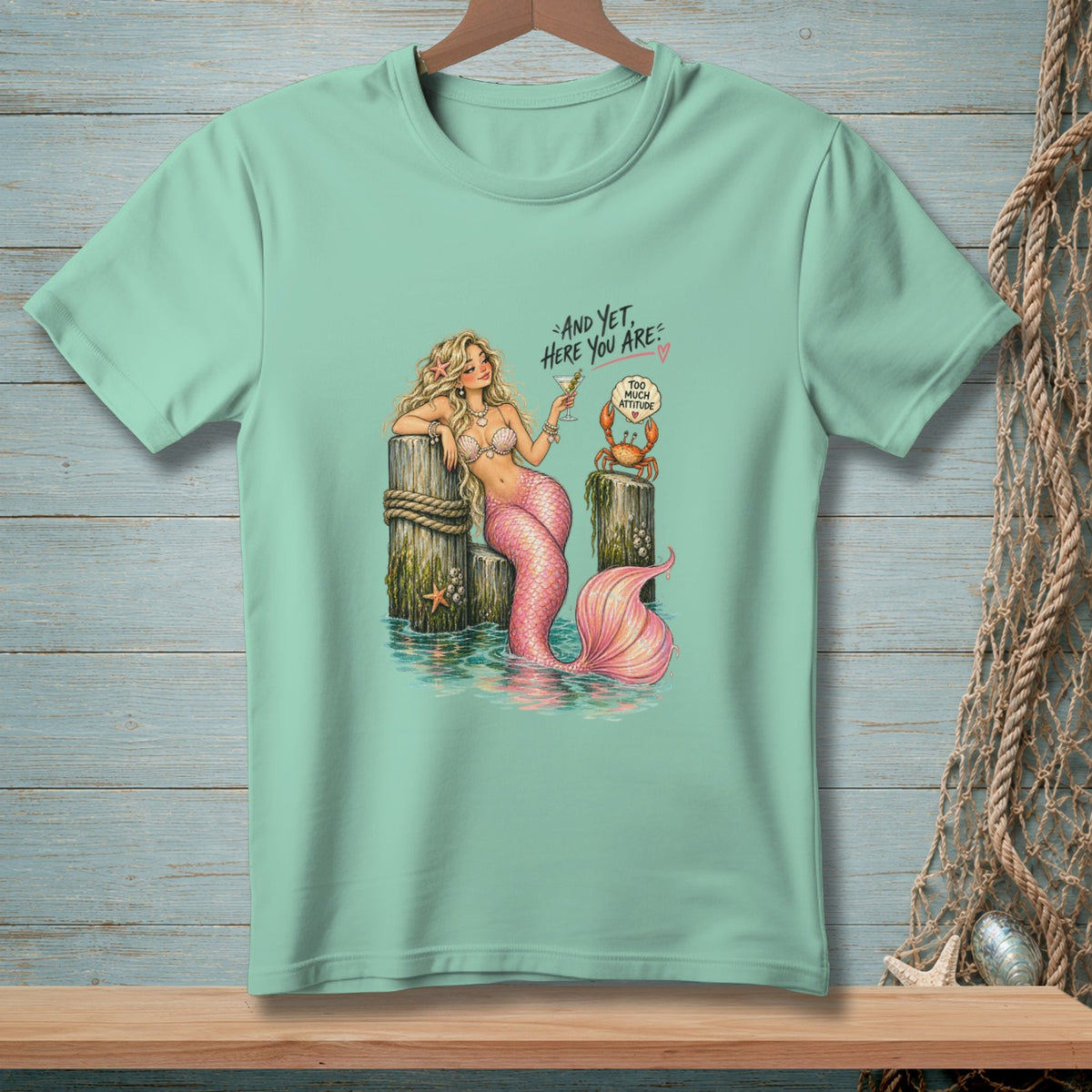 Mint t-shirt with mermaid, crab, and text "And yet, here you are."