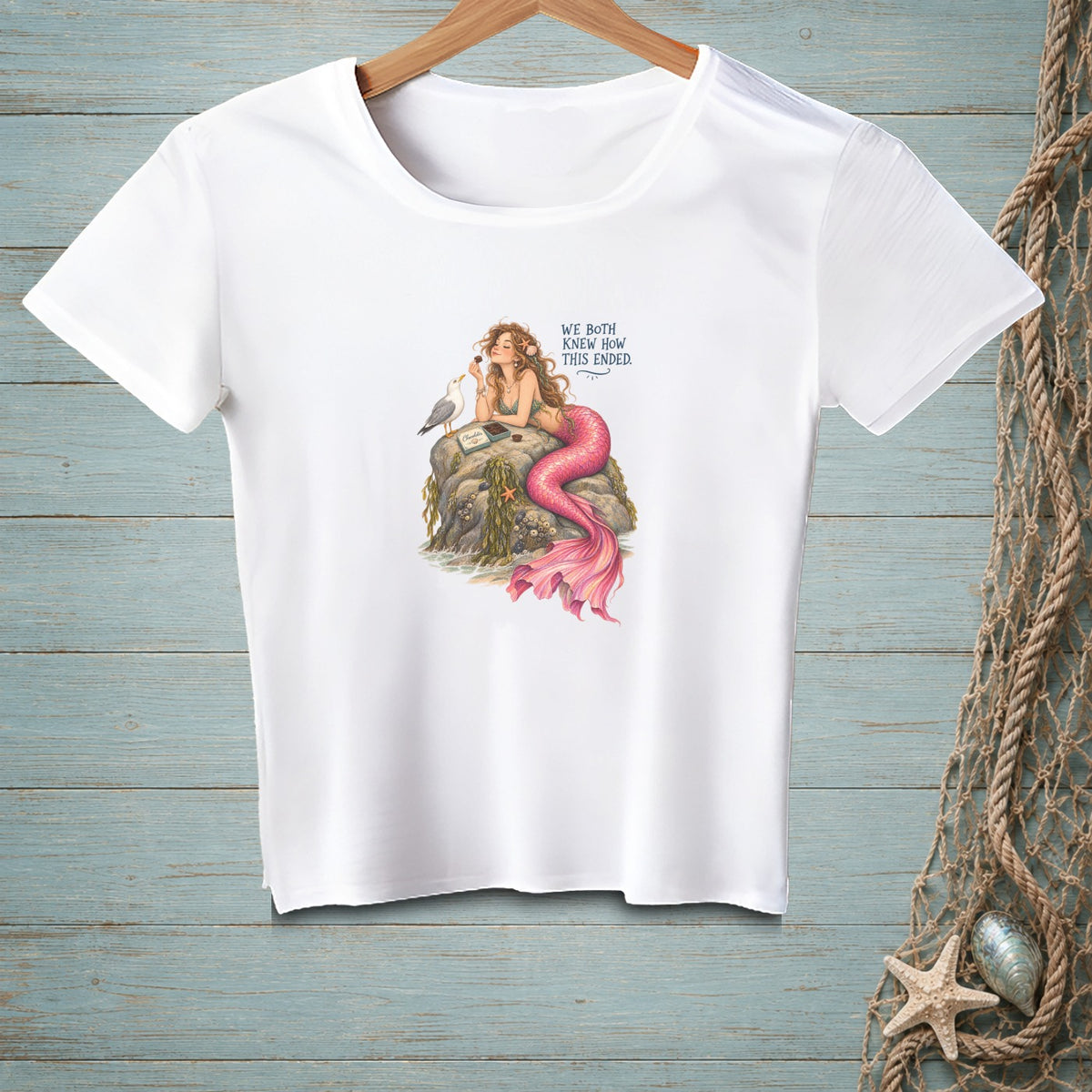 Mermaid on rock with a seagull and chocolate, text reads "We Both Knew How This Ended".