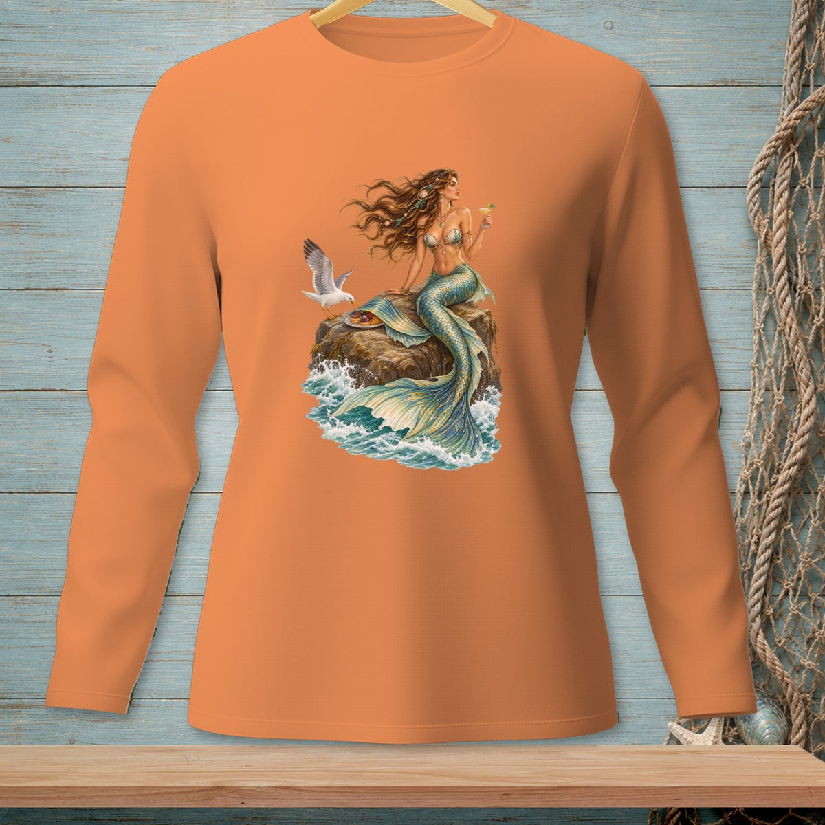 Mermaid sitting on a rock with a drink, seagull and waves on an orange long-sleeve shirt.