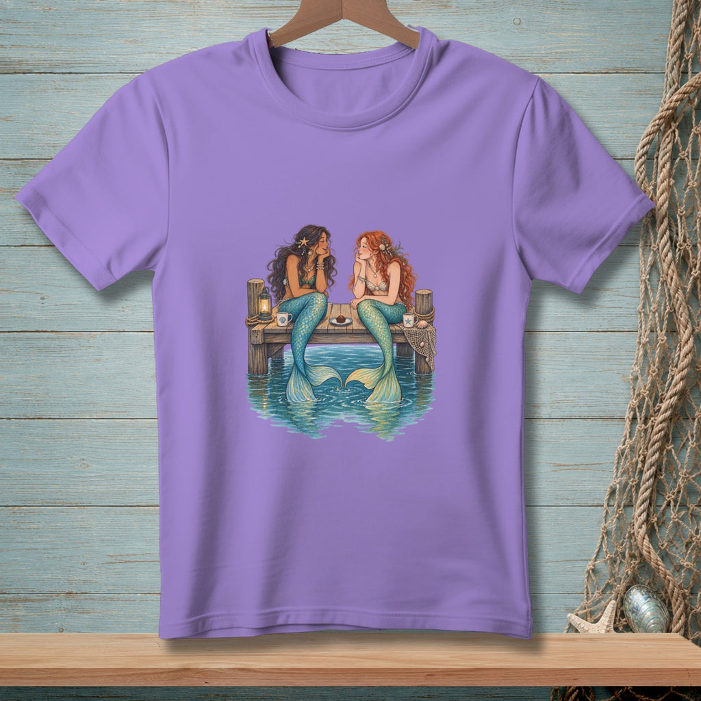 Two mermaids sit on a dock talking, with tails in the water.