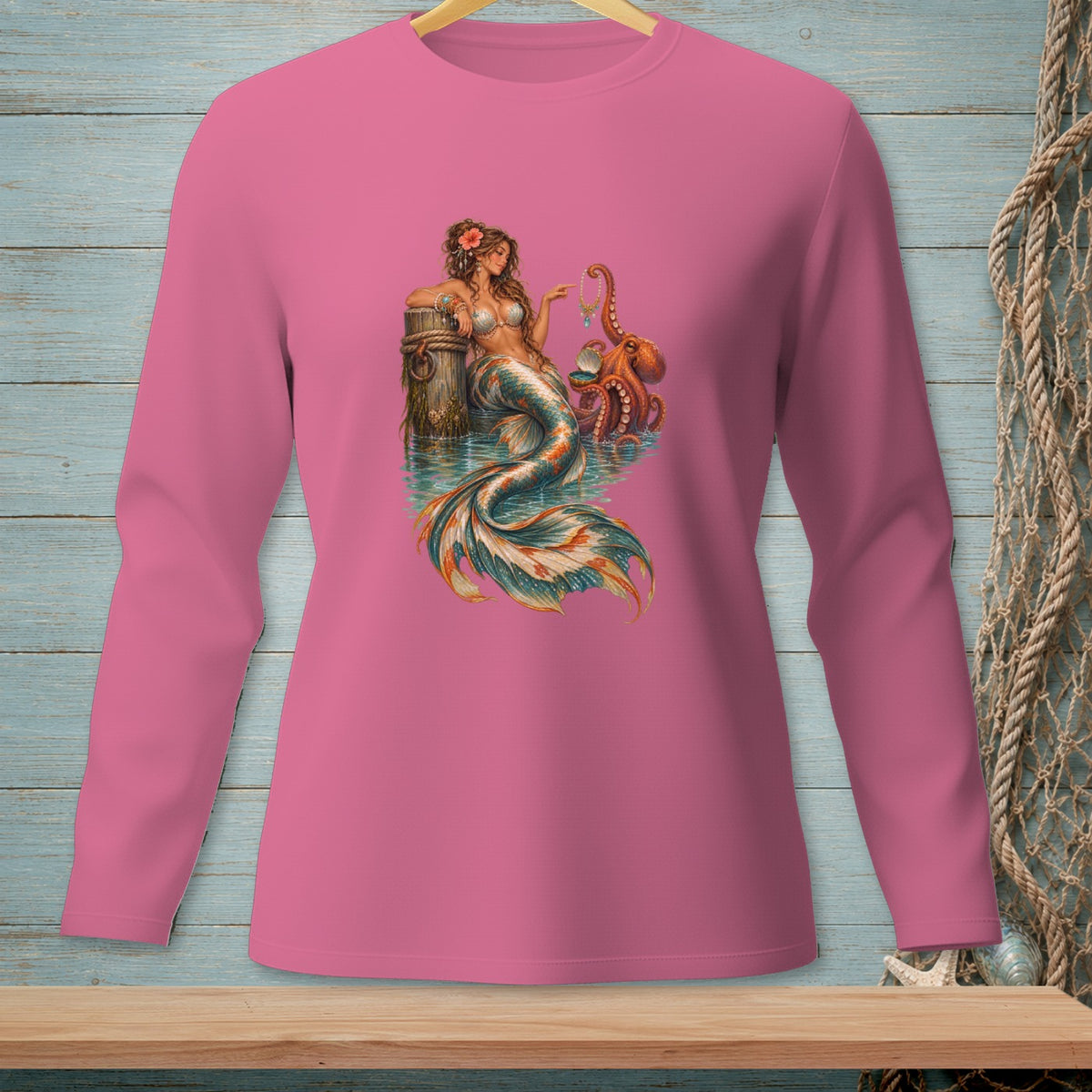 Long-sleeve pink shirt with mermaid and octopus graphic on wood plank background.