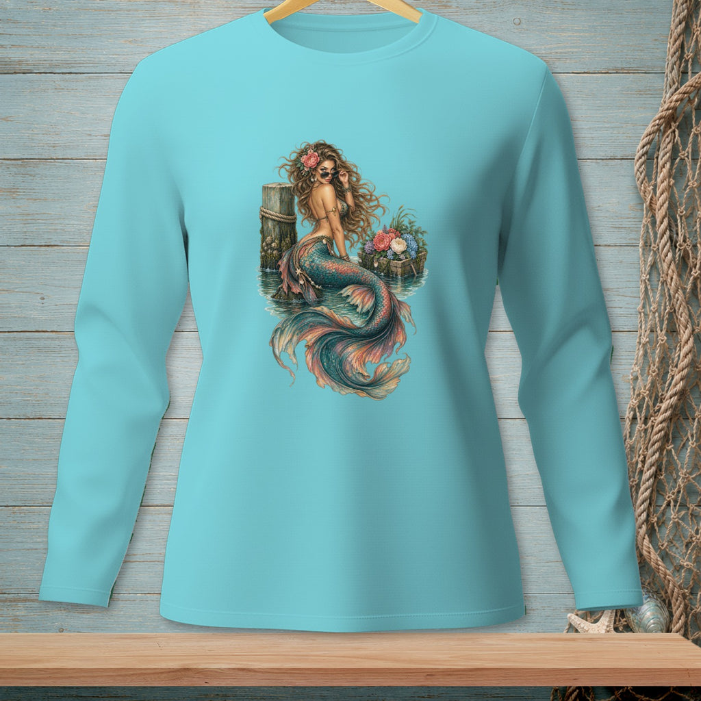 Mermaid with sunglasses and flowers sitting on a dock with a basket of flowers.
