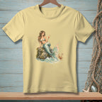 Light yellow t-shirt with a watercolor print of a mermaid holding a drink by the sea.