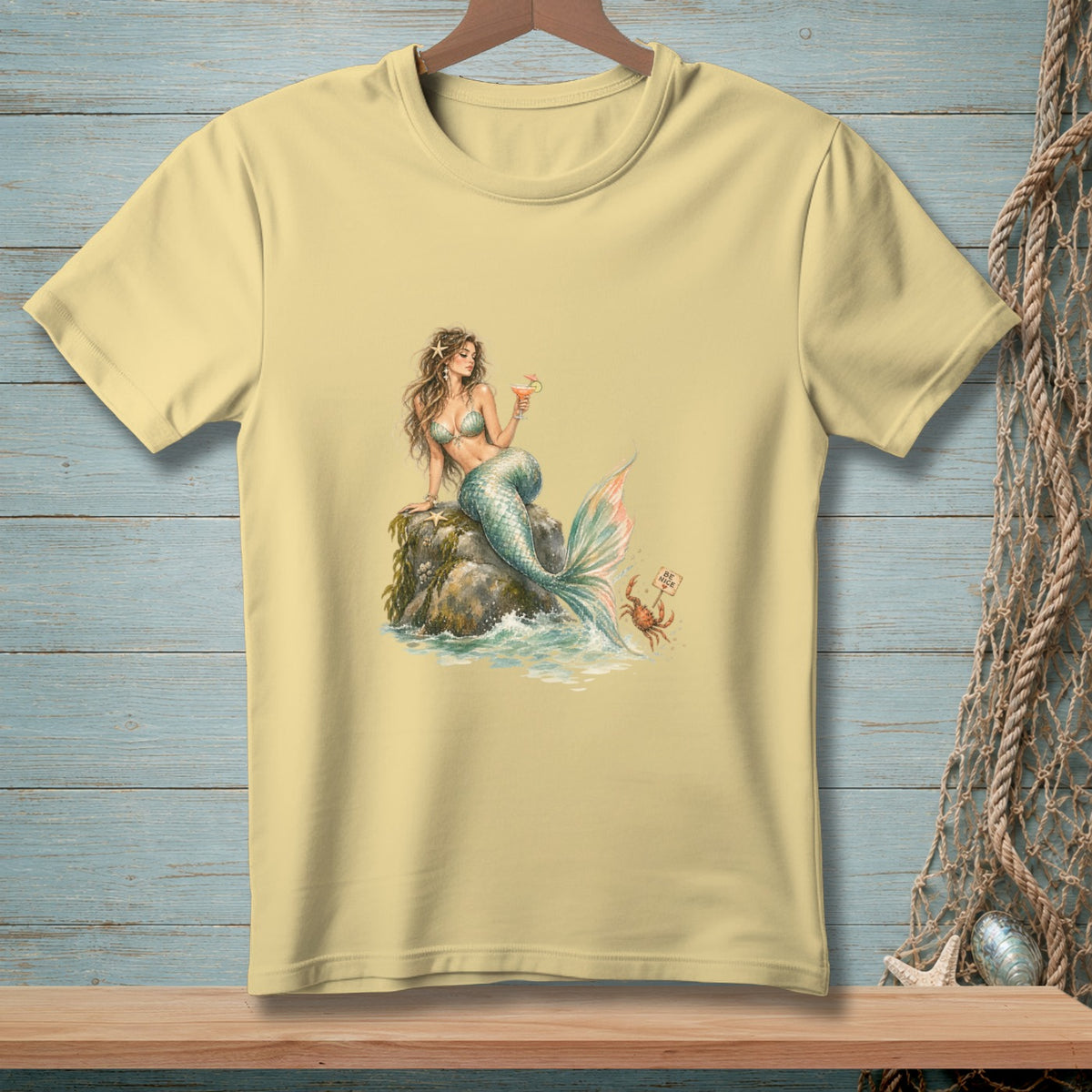 Light yellow t-shirt with a watercolor print of a mermaid holding a drink by the sea.
