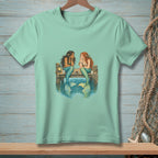Two mermaids sit on a wooden pier, enjoying coffee by the water.