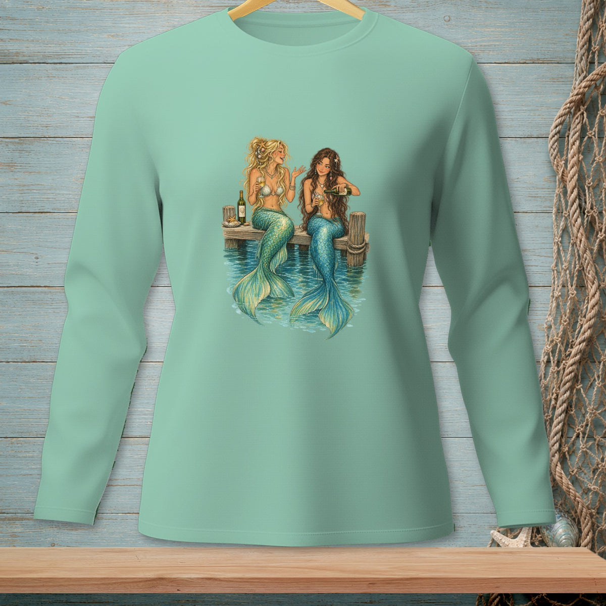 Two mermaids with colorful tails sit on a dock, drinking wine.
