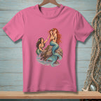 Two mermaids on a rock by the sea, one holding a seashell.