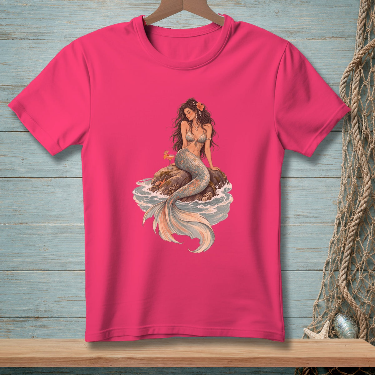 Pink t-shirt featuring a mermaid with a drink sitting on a rock.