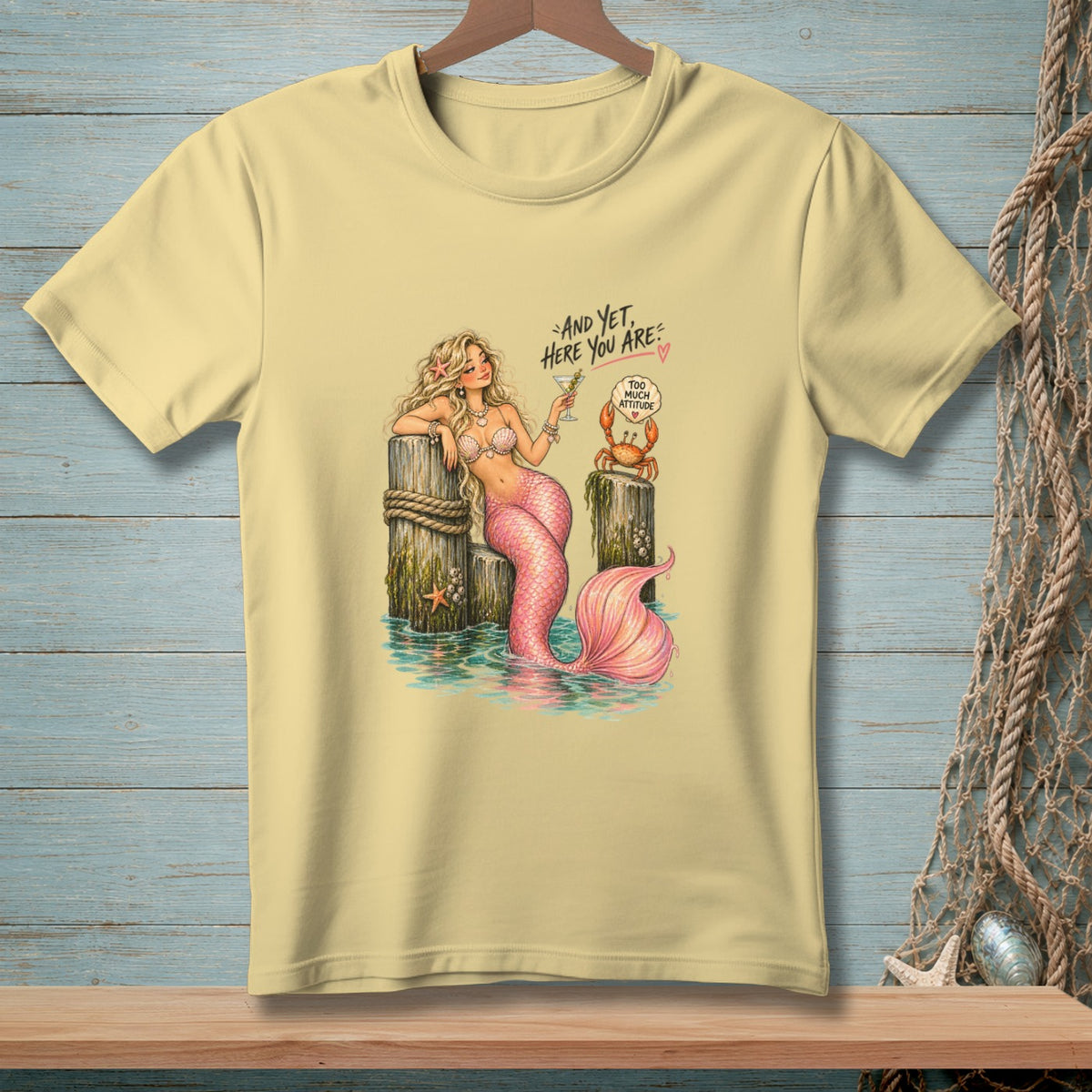 Yellow t-shirt with a mermaid, crab, and text "And yet, here you are".