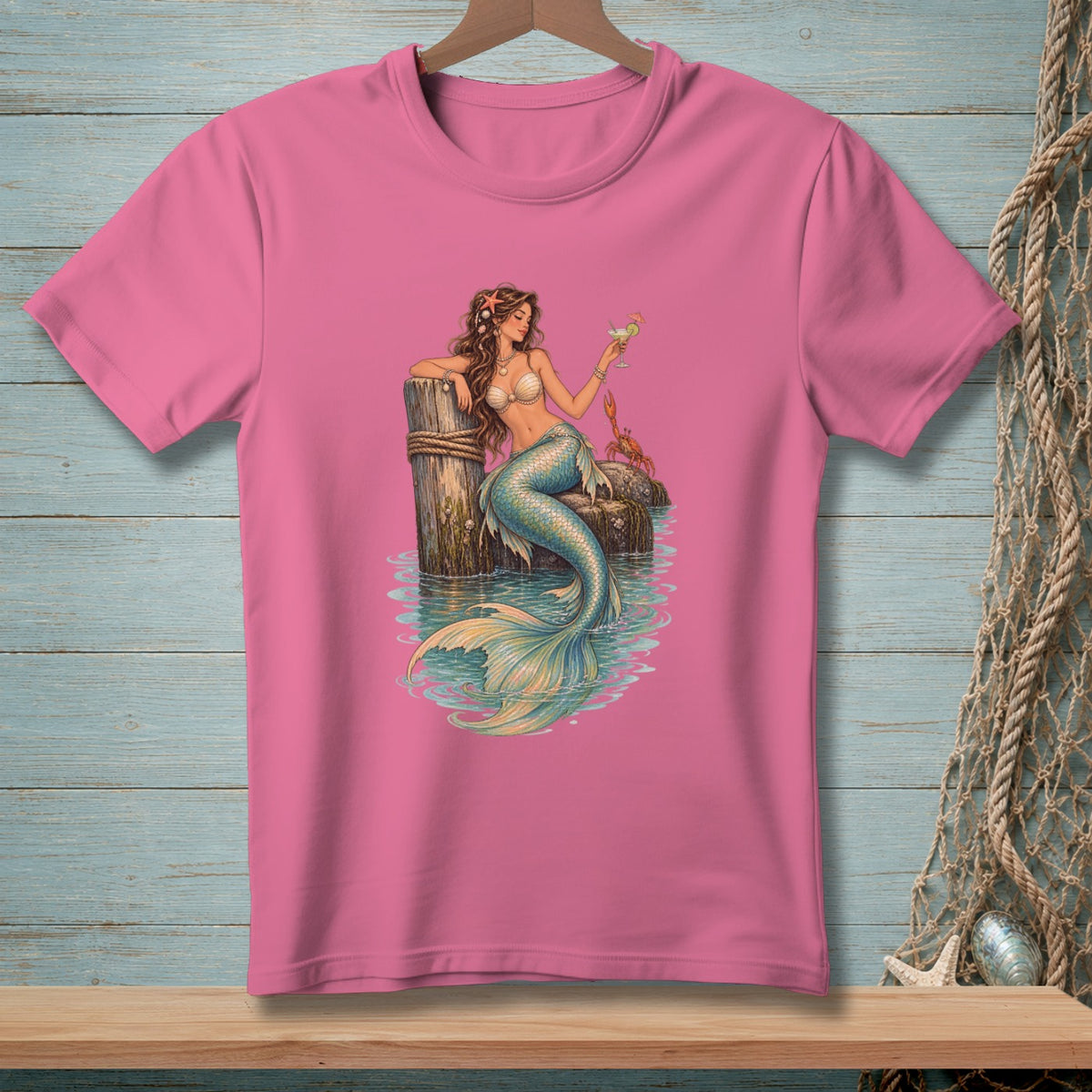 Pink t-shirt with a mermaid holding a cocktail on a dock with a crab.