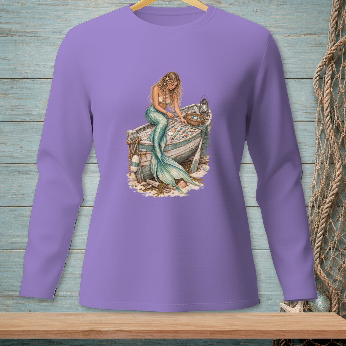 Purple long-sleeve shirt with a watercolor mermaid sitting on a weathered boat filled with shells.