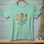 Three mermaids with champagne flutes in water on a mint green t-shirt.