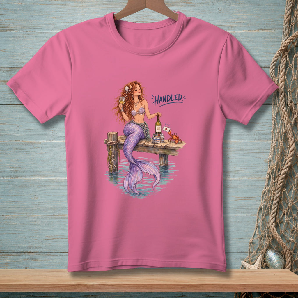 Pink t-shirt with mermaid and crab on a dock, text reads "Handled."