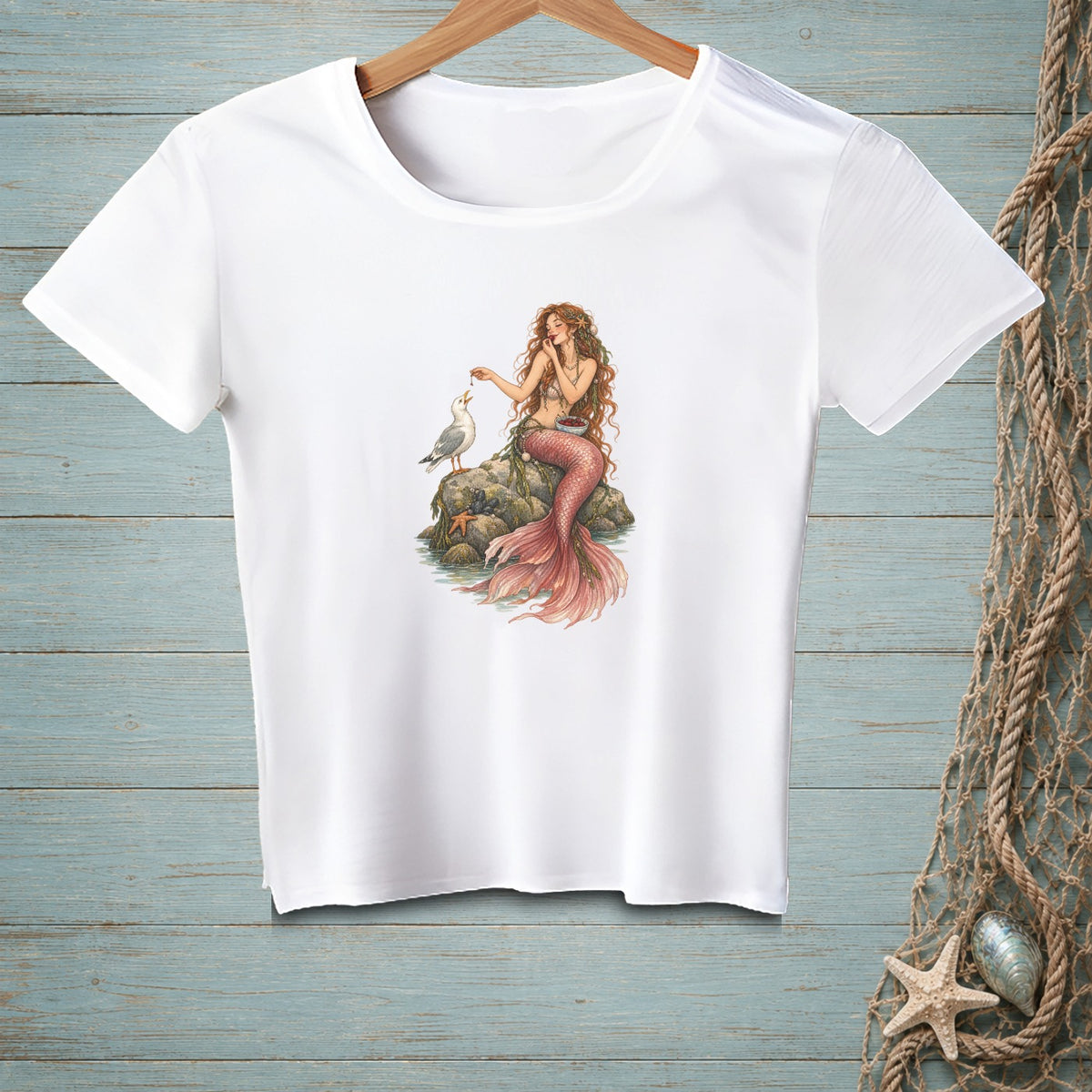White t-shirt featuring a mermaid feeding a seagull on a rock.