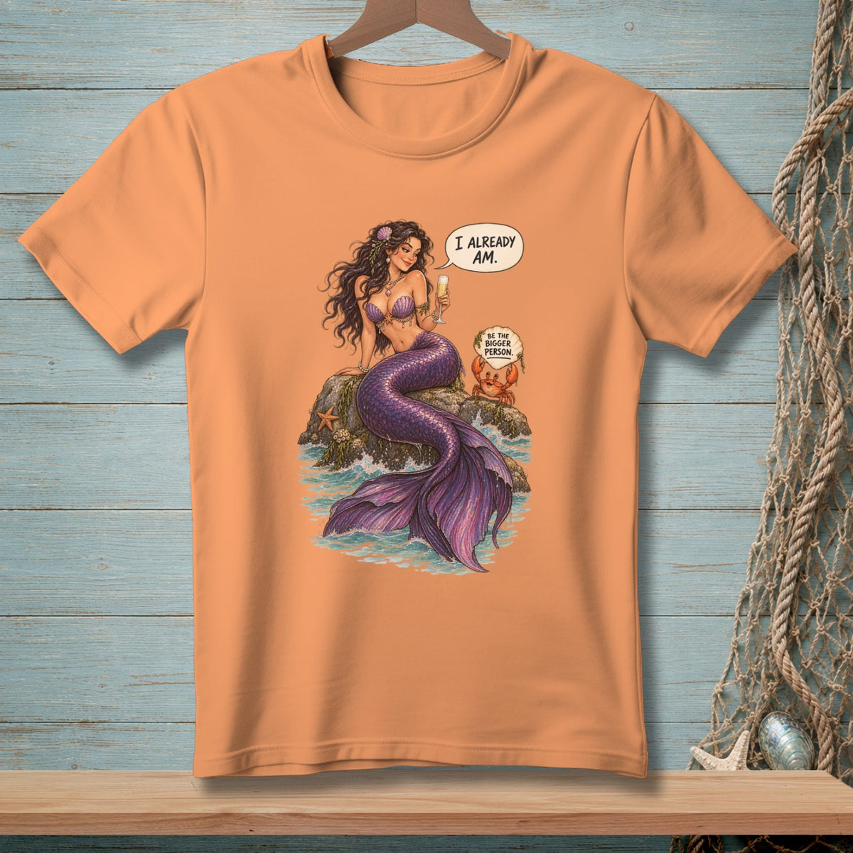 Peach t-shirt with a mermaid holding a drink and a crab saying "I already am."