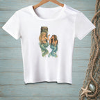 White t-shirt with illustration of two mermaids by a wooden post in water.