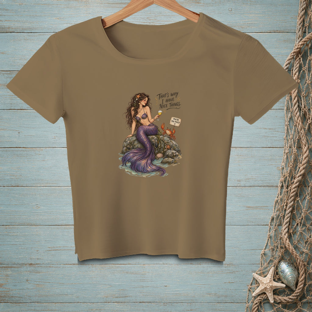 A mermaid sits on rocks with a crab, holding a drink, with text.