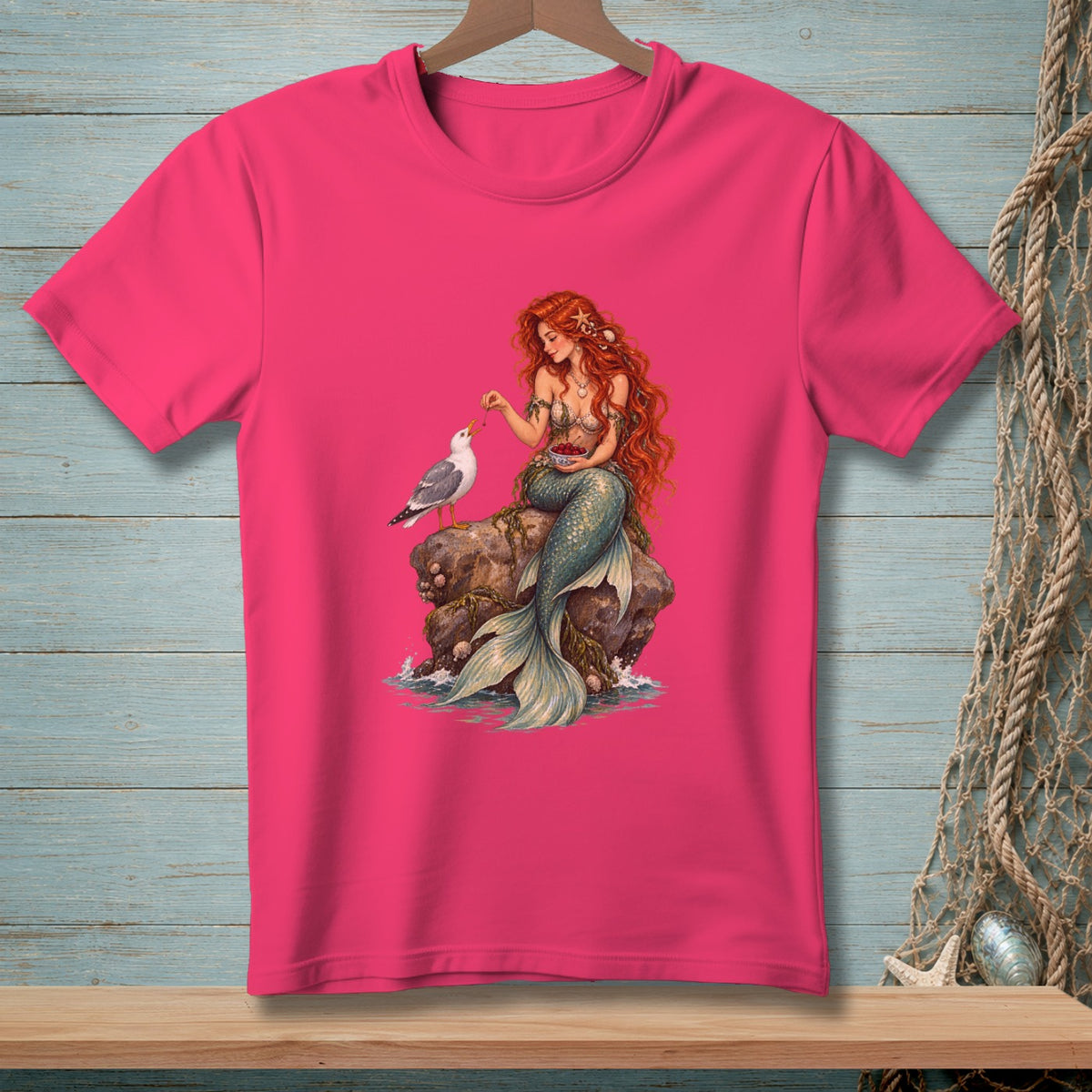 Mermaid on a rock feeding a bird, with a bowl of berries, printed on a pink t-shirt.