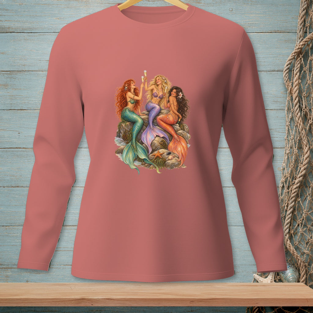 Three mermaids with colorful tails sit on rocks holding champagne flutes.