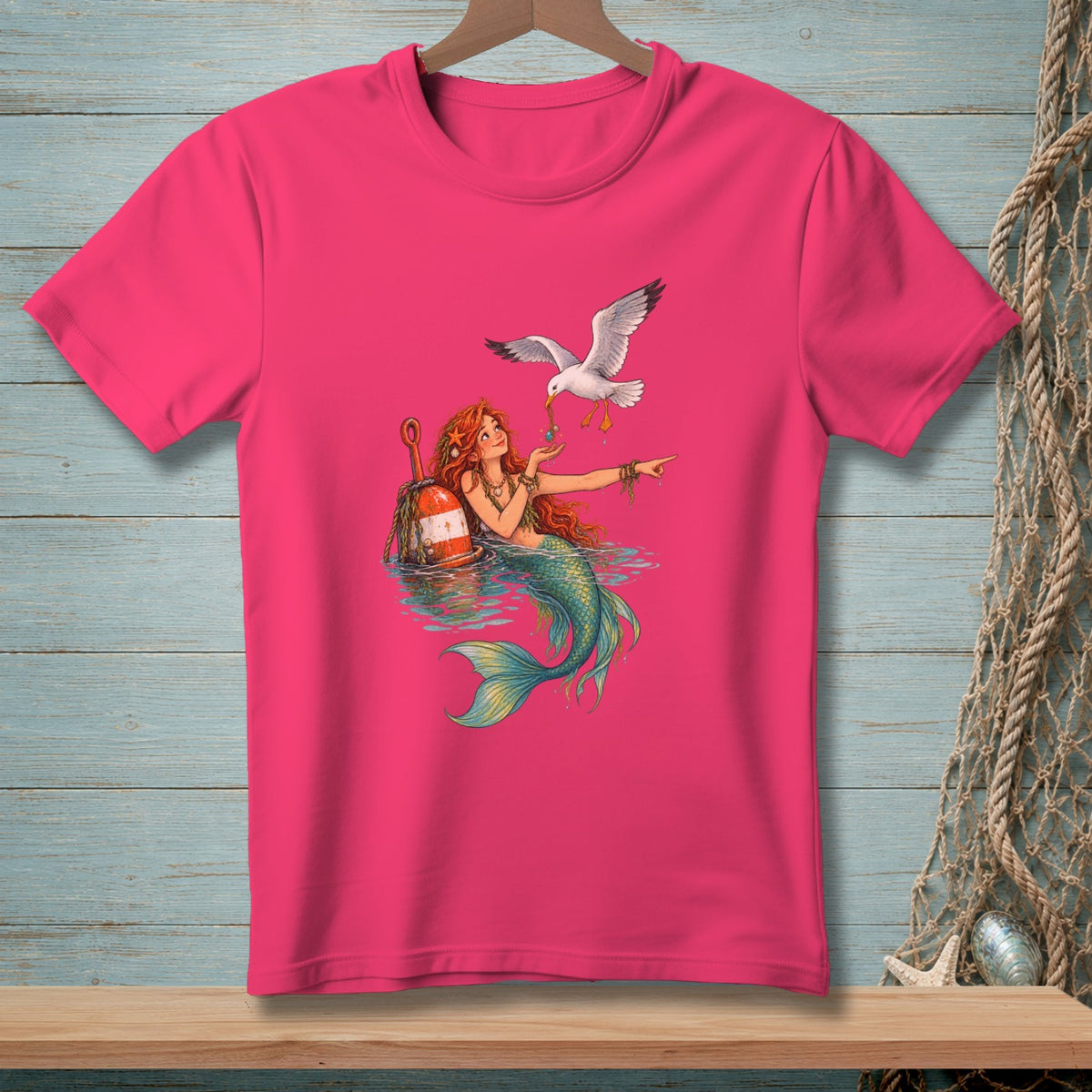 Pink t-shirt with mermaid holding beads for a seagull, near a buoy.