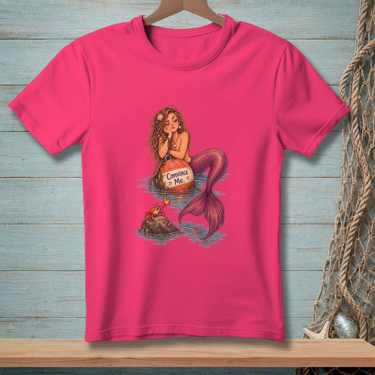 Pink t-shirt featuring a mermaid on a buoy with text "Convince Me." and a crab.