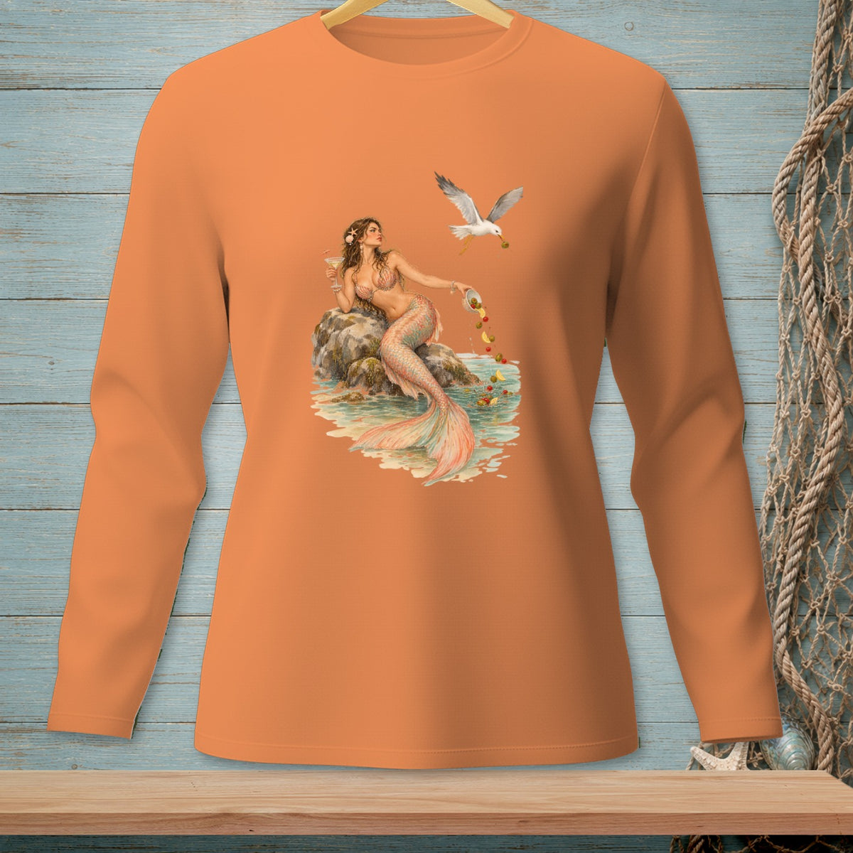 Long sleeve orange shirt with a mermaid feeding a seagull by the sea.