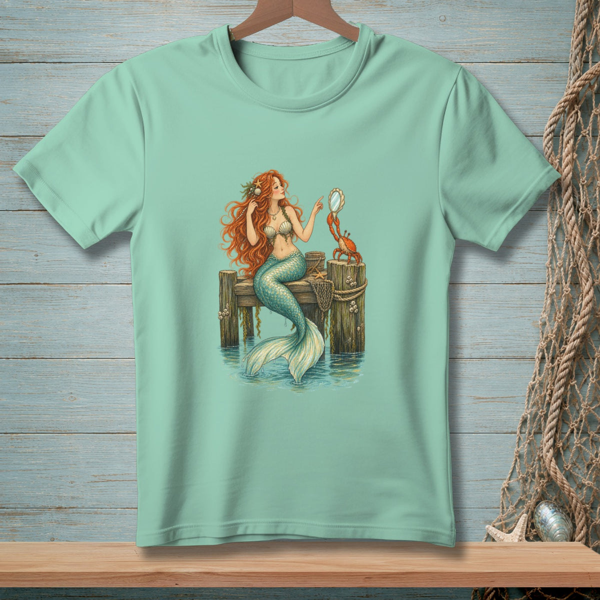 Mint t-shirt with illustration of mermaid on pier with crab and mirror.