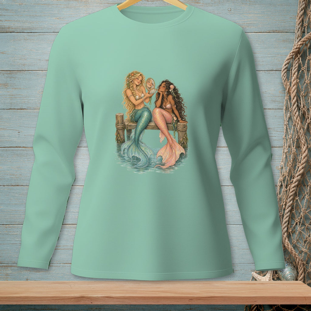 Two mermaids sitting on a wooden pier, one looking in a mirror.