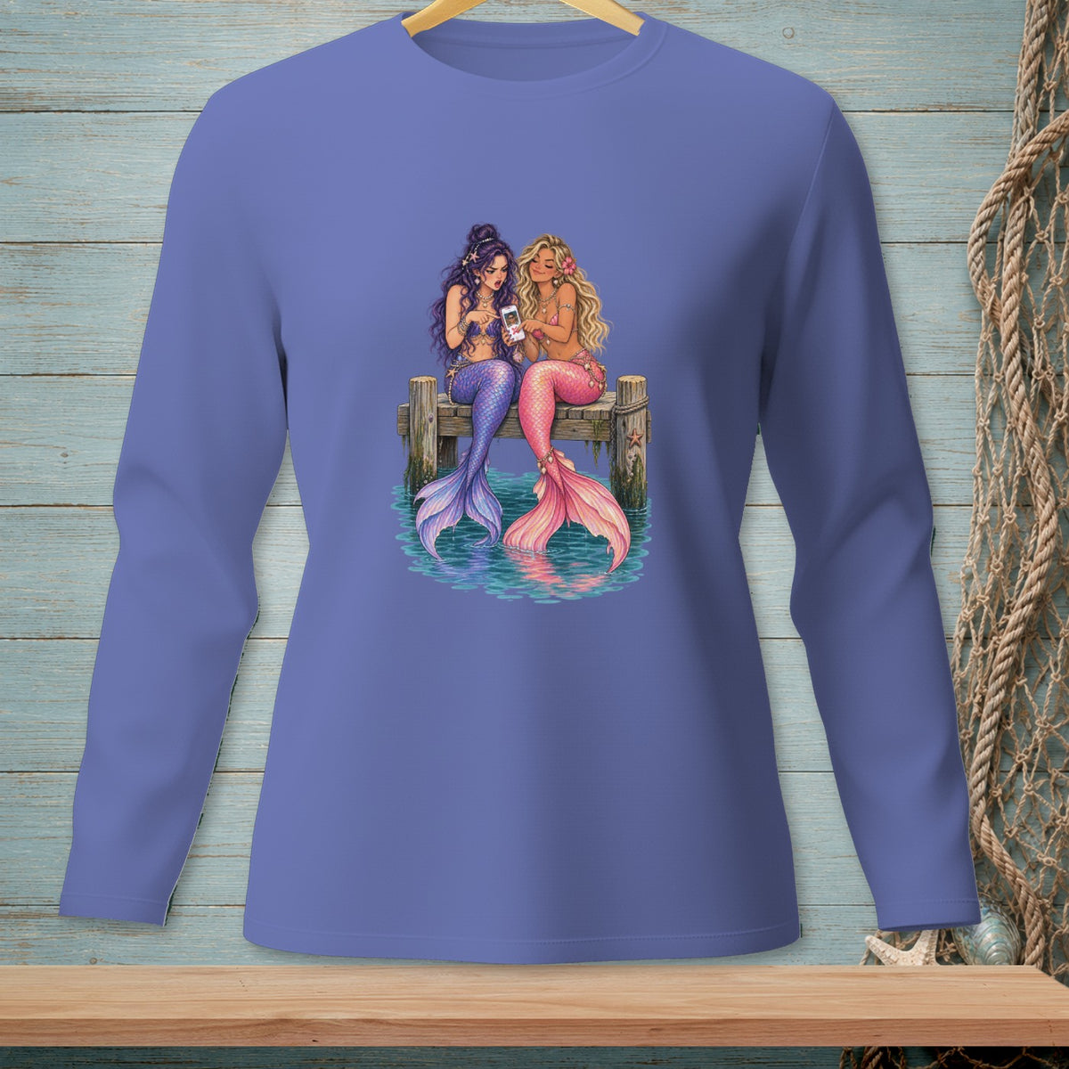 Two mermaids with colorful tails sit on a dock looking at a phone.