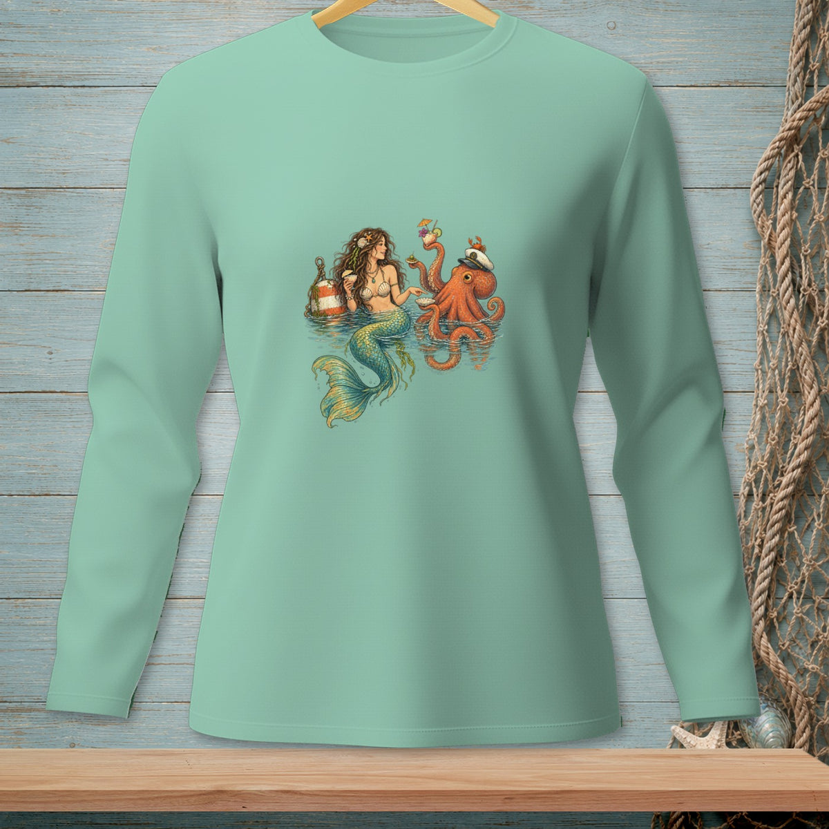 Mermaid and octopus drinking cocktails with a buoy on a light teal long-sleeve shirt.