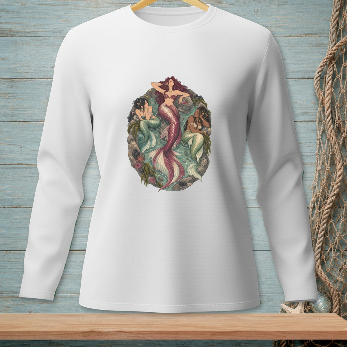 White long-sleeve shirt featuring an oval graphic of three mermaids surrounded by rocks and seaweed.
