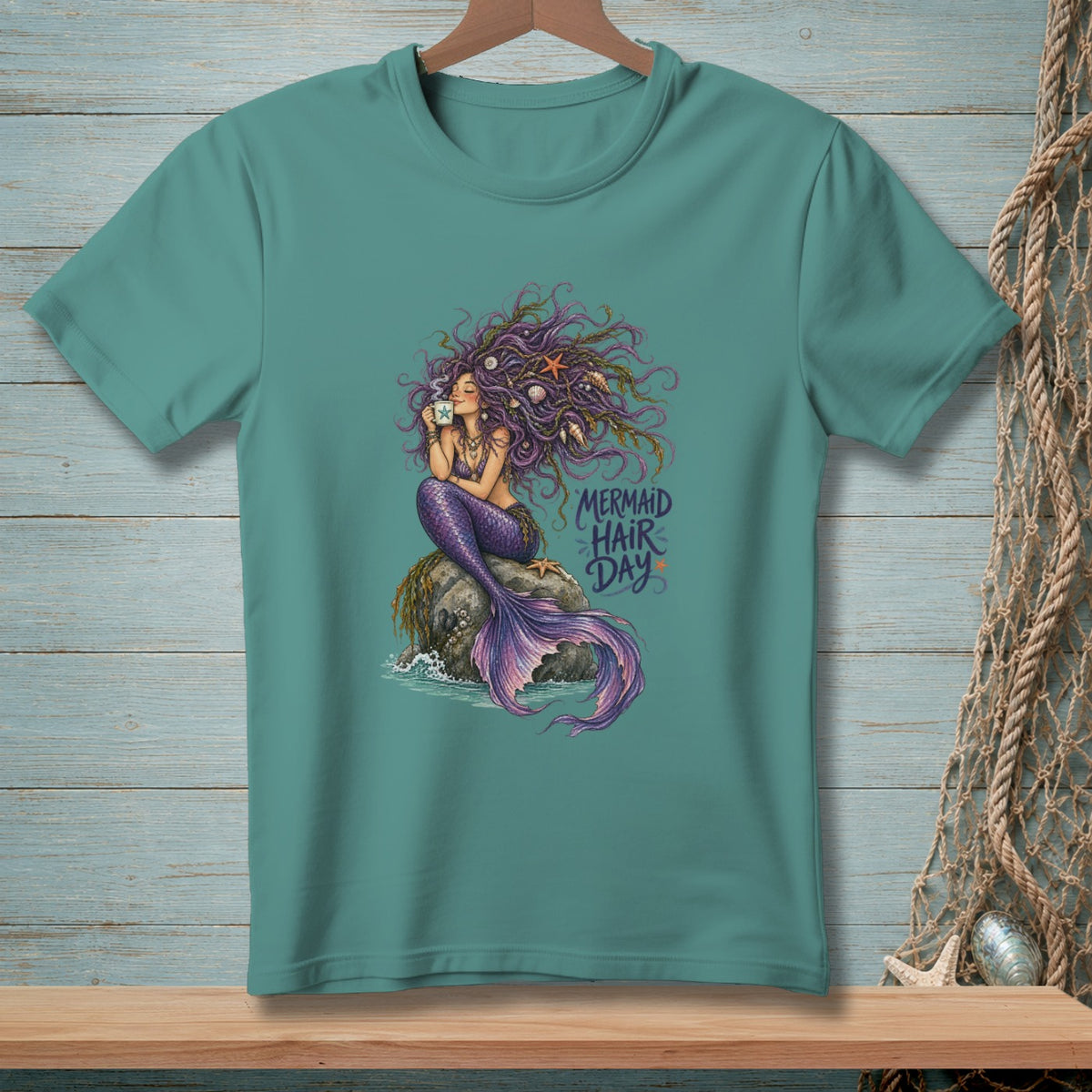 Mermaid with purple hair sitting on a rock drinking coffee, text reads "Mermaid Hair Day".
