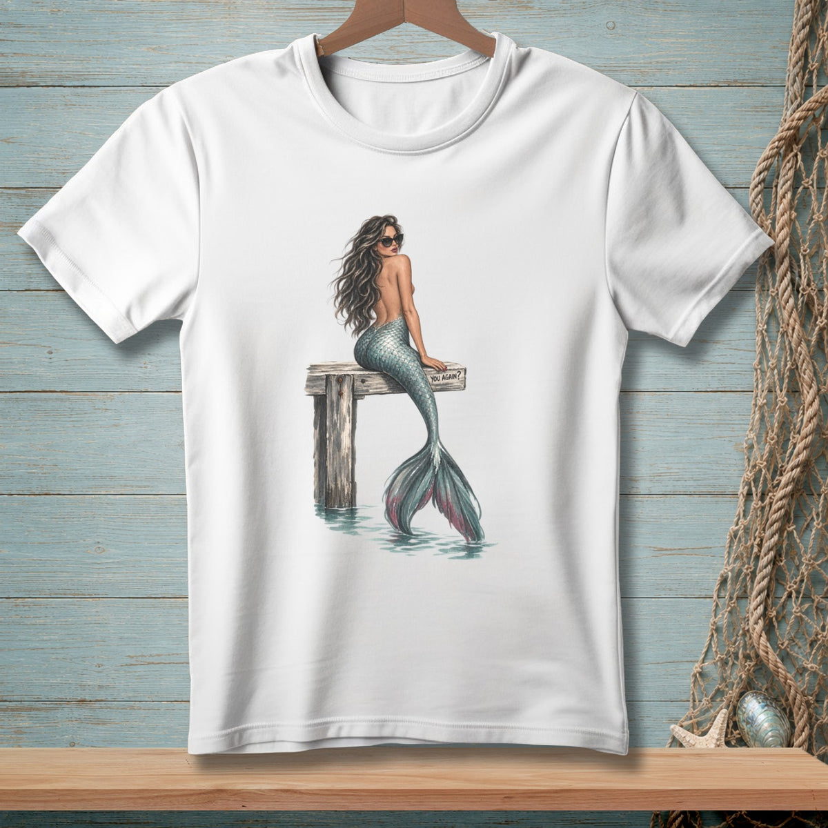 White t-shirt with illustration of a mermaid wearing sunglasses sitting on a dock.