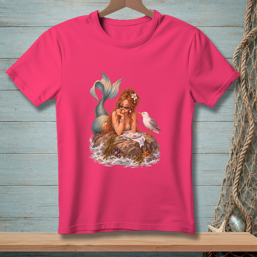 Pink t-shirt with a mermaid and seagull on a rock by the ocean.