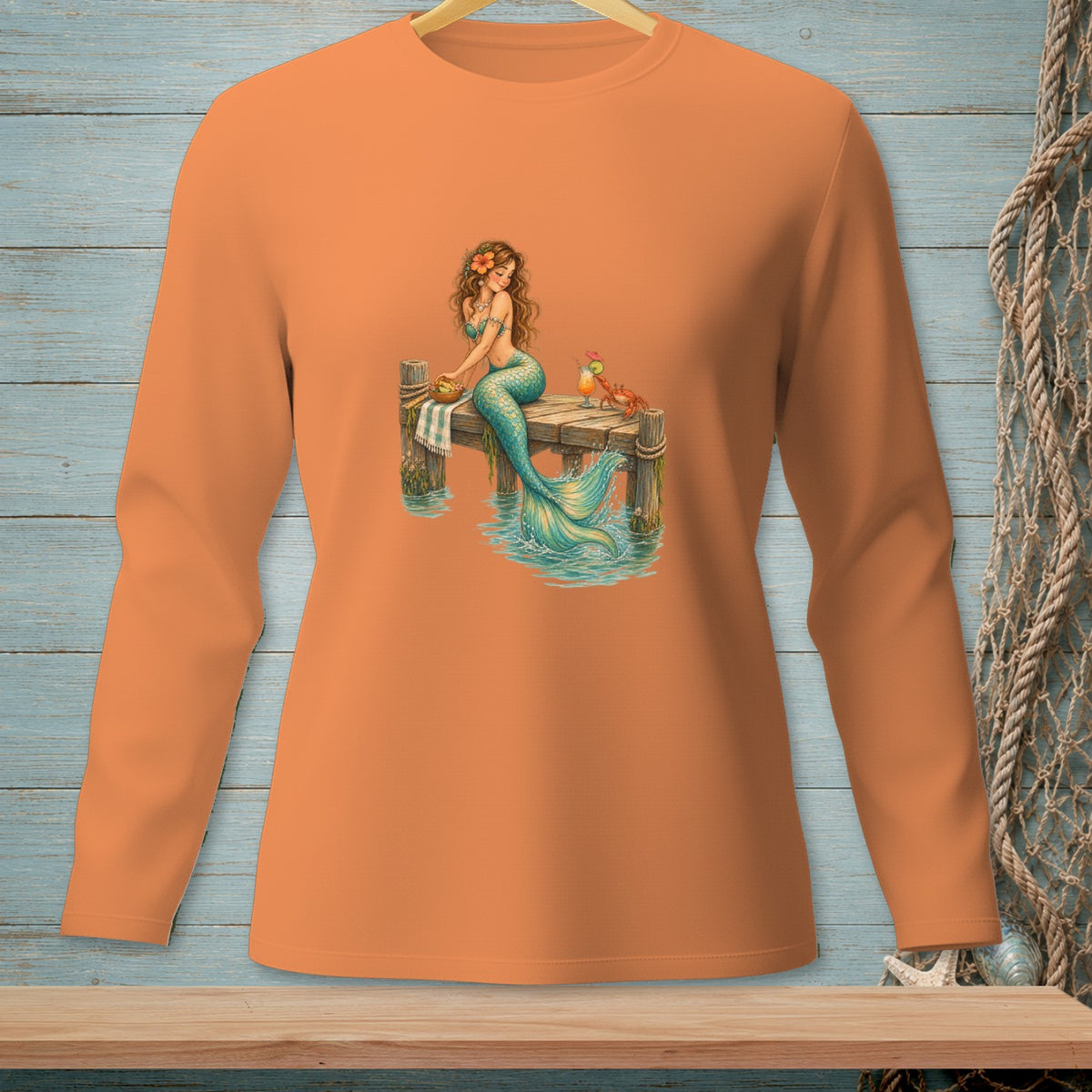 Orange long-sleeve shirt with a mermaid sitting on a dock with drinks and a crab.