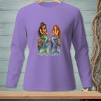 Two mermaids sit on a dock sharing a bowl, with their tails in the water.
