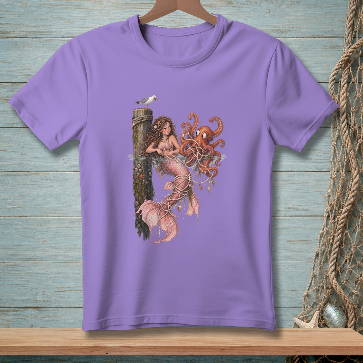 Purple t-shirt with mermaid and octopus graphic on a wooden background.
