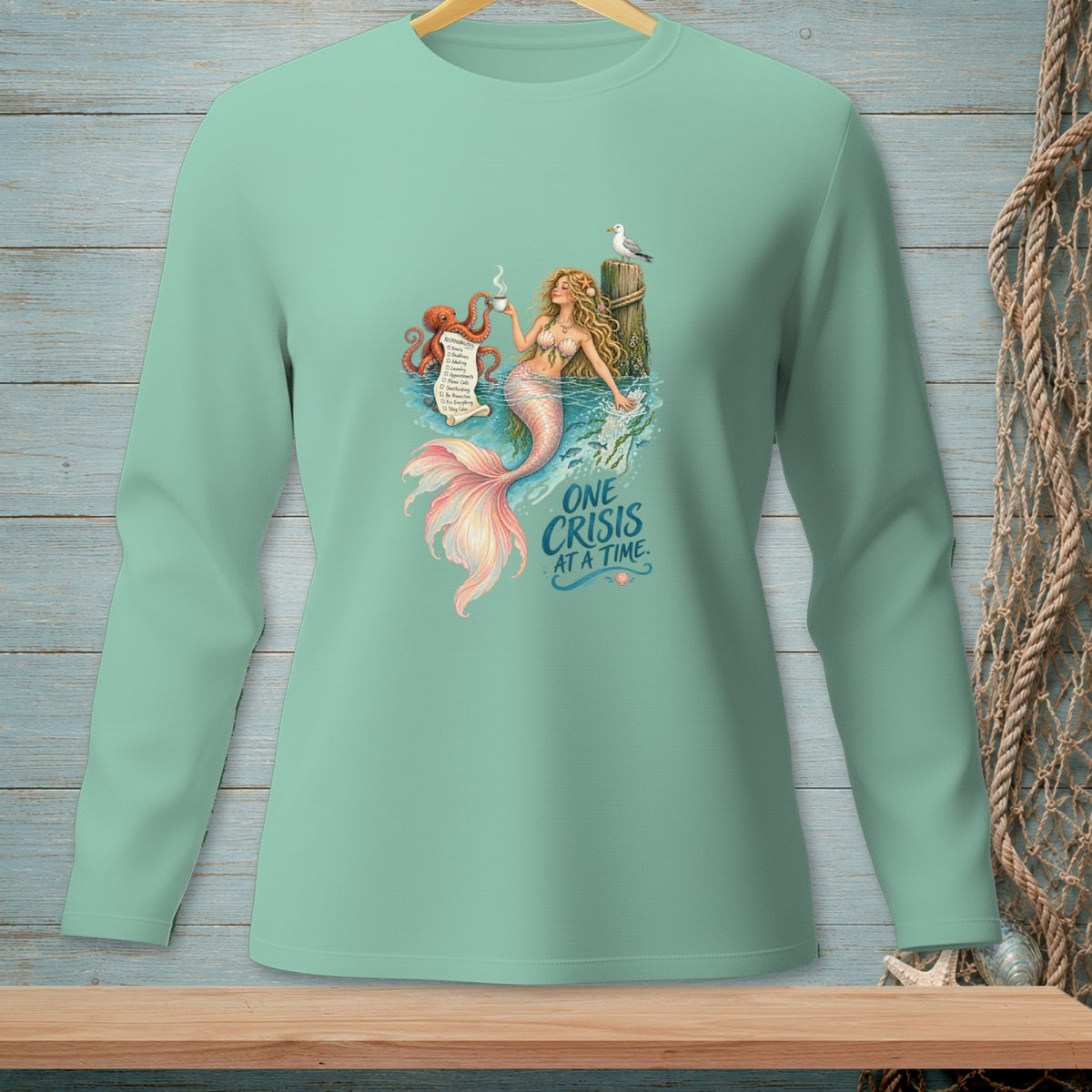 Mint green long-sleeve shirt with mermaid, octopus, and "One crisis at a time" text.
