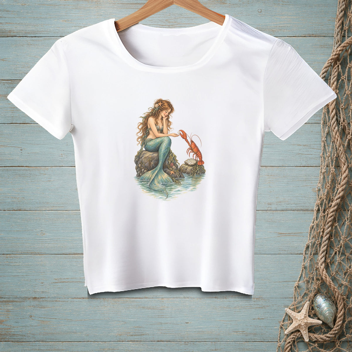 White t-shirt with mermaid and lobster artwork on a rock in water.