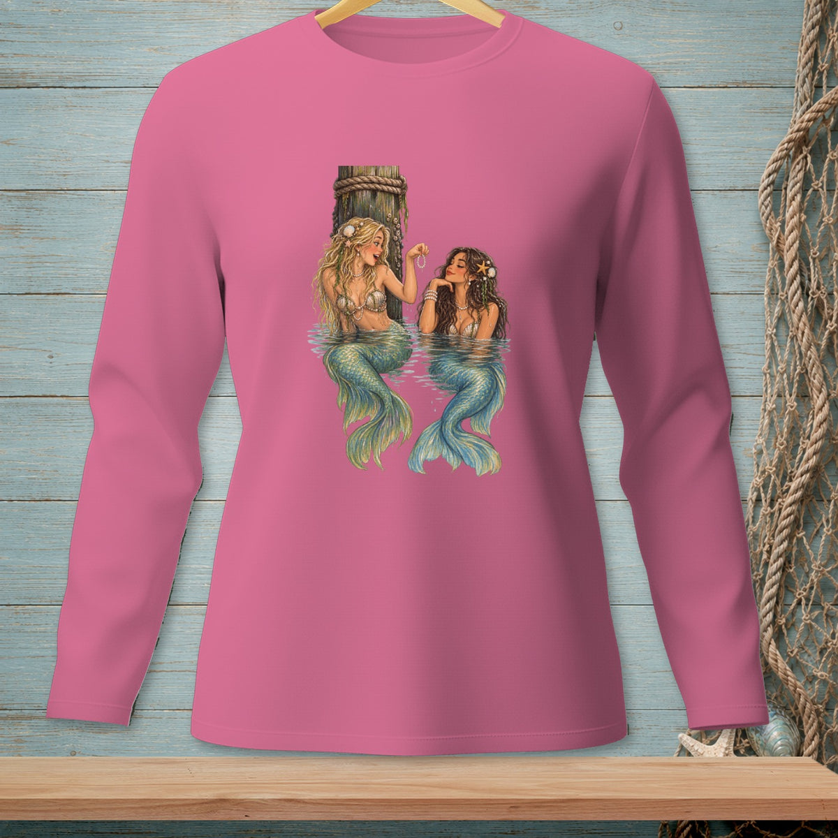 Two mermaids sit in water by a wooden post, one with blonde hair and one with dark hair.