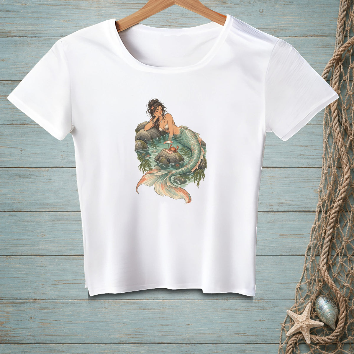 White t-shirt with a graphic of a mermaid resting on rocks in water, with a small crab.
