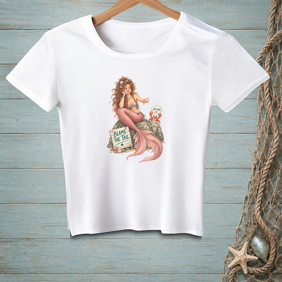 White t-shirt with a mermaid sitting on a rock with a crab and a sign reading "BLAME THE TAIL."
