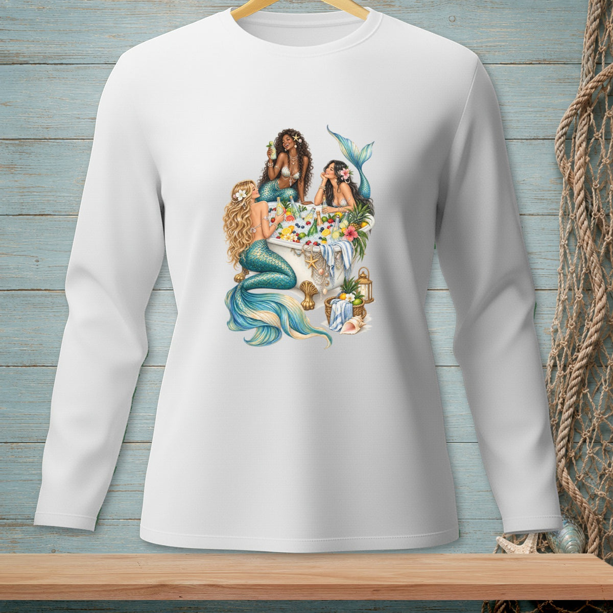 A white long-sleeved shirt displays a vibrant graphic of three mermaids relaxing in a tropical bathtub.
