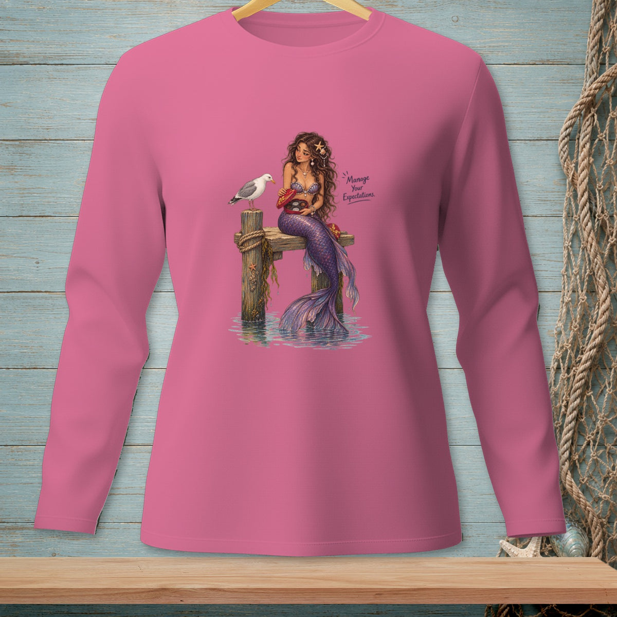Pink long-sleeve shirt with a mermaid and seagull, featuring text "Manage Your Expectations."