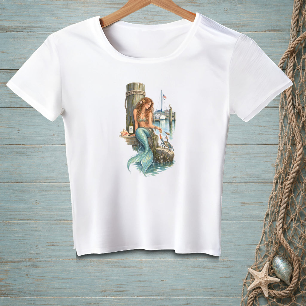 White t-shirt with mermaid on dock with crab and sailboats in background.
