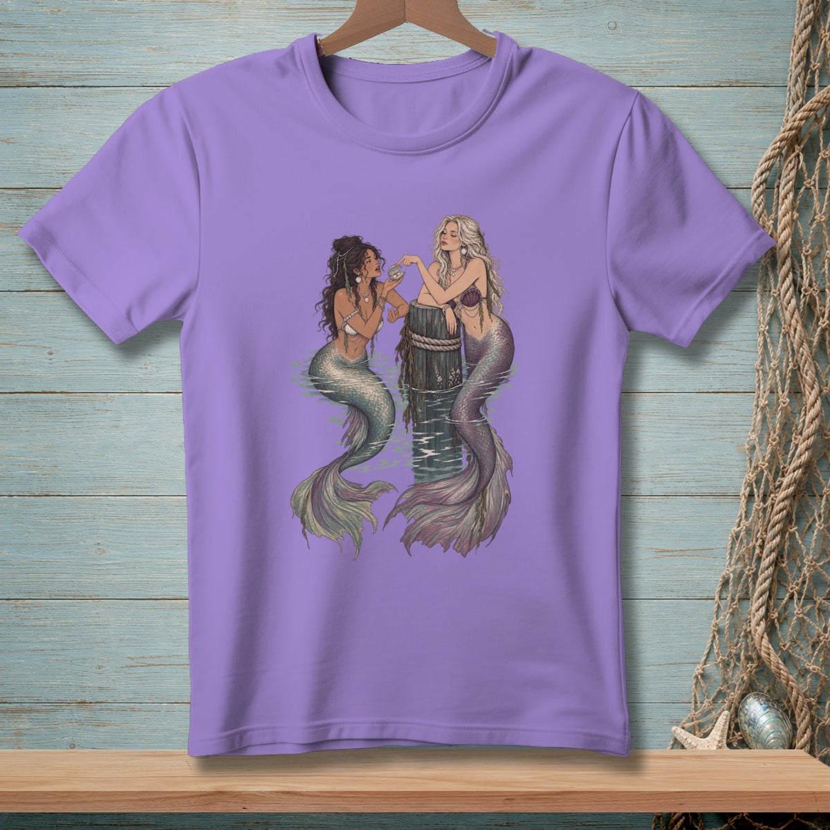 Purple t-shirt with two mermaids sitting on a wooden post in the water.