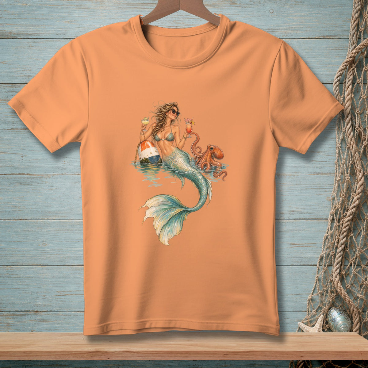Orange t-shirt with a graphic of a mermaid holding cocktails next to a buoy and octopus.