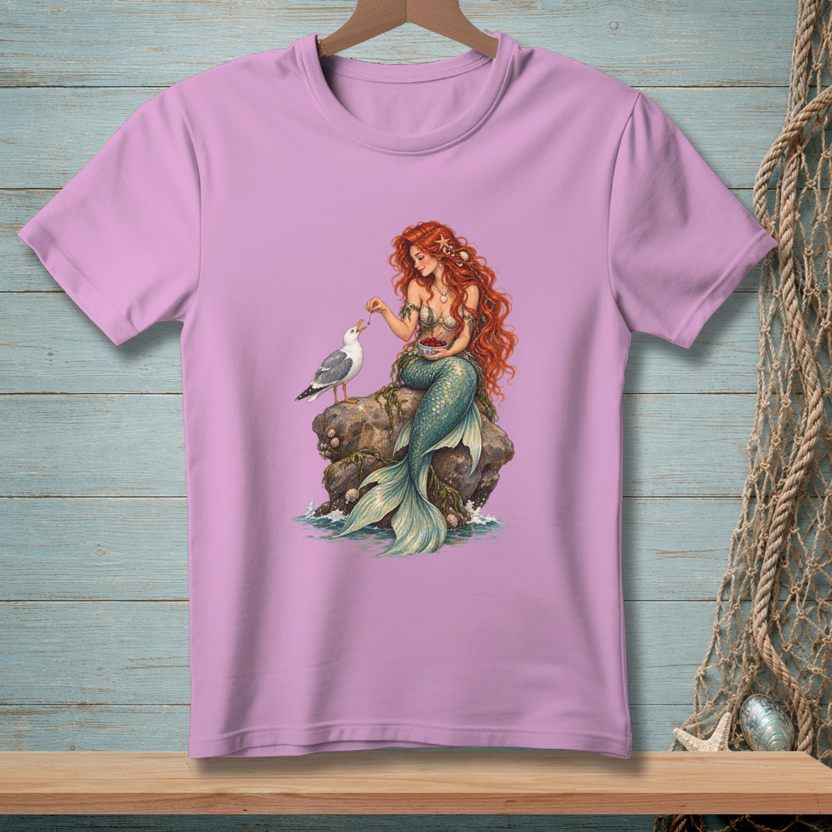 Purple t-shirt featuring a mermaid feeding berries to a seagull on a rock.