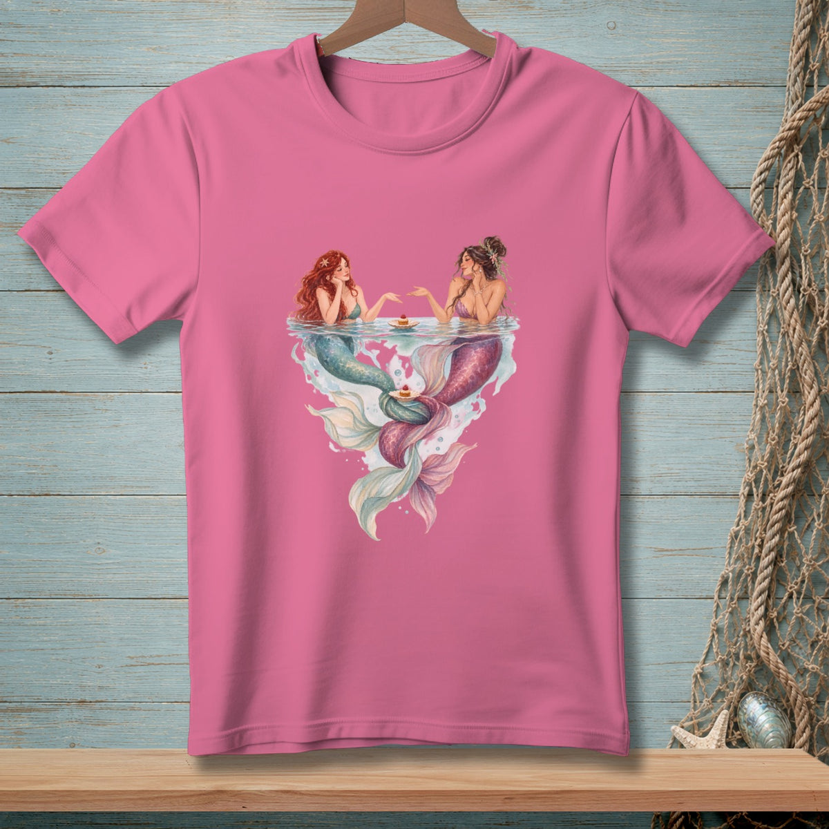 Two mermaids with tails in pastel colors share cupcakes at the water's surface.
