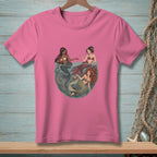 Three mermaids interact within a circular frame on a pink t-shirt.